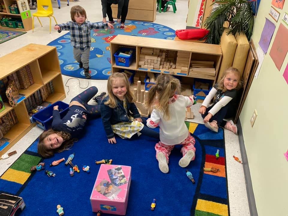 Children playing on a blue rug in a classroom