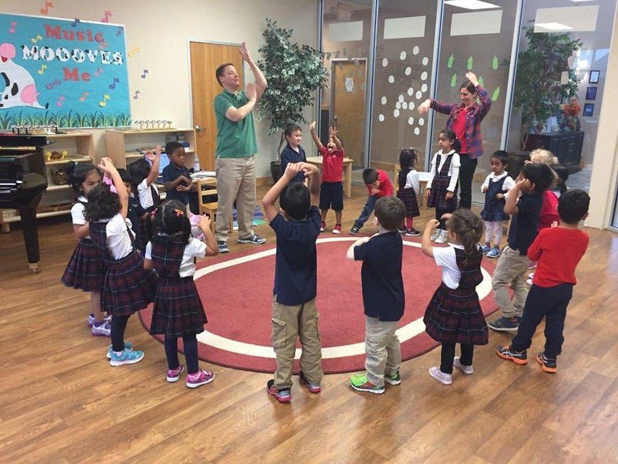 Adults and children standing in a circle with arms raised in a classroom