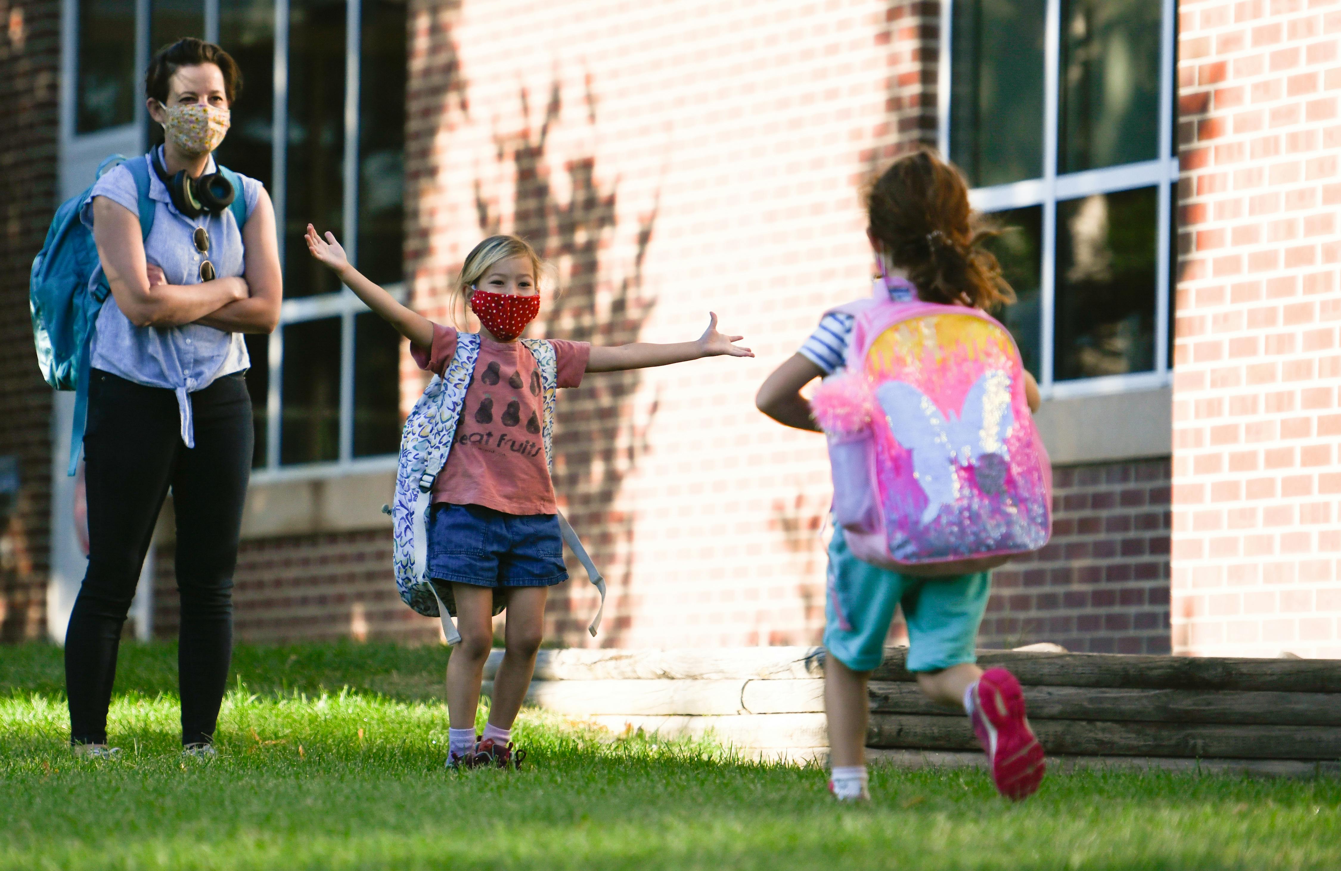 Person and two children with backpacks and face masks outside a building