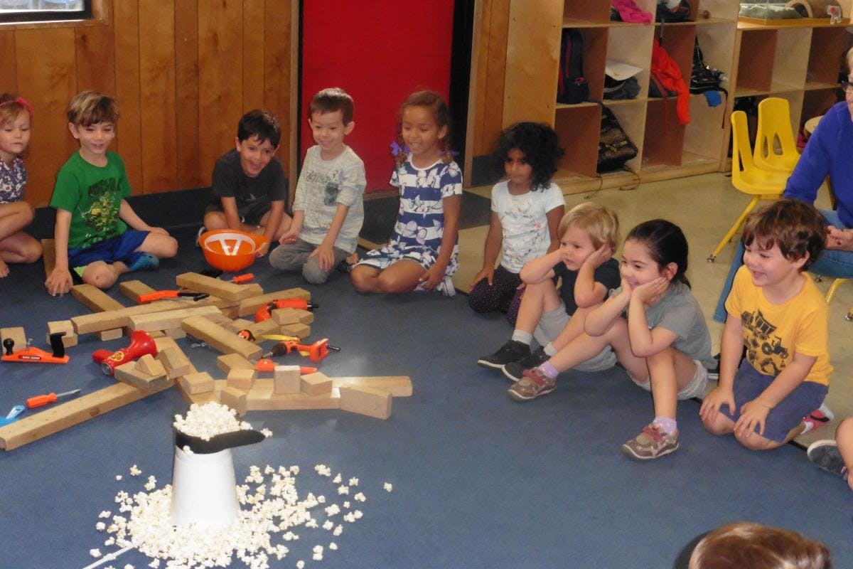 Children sitting on the floor around a structure made of wooden blocks