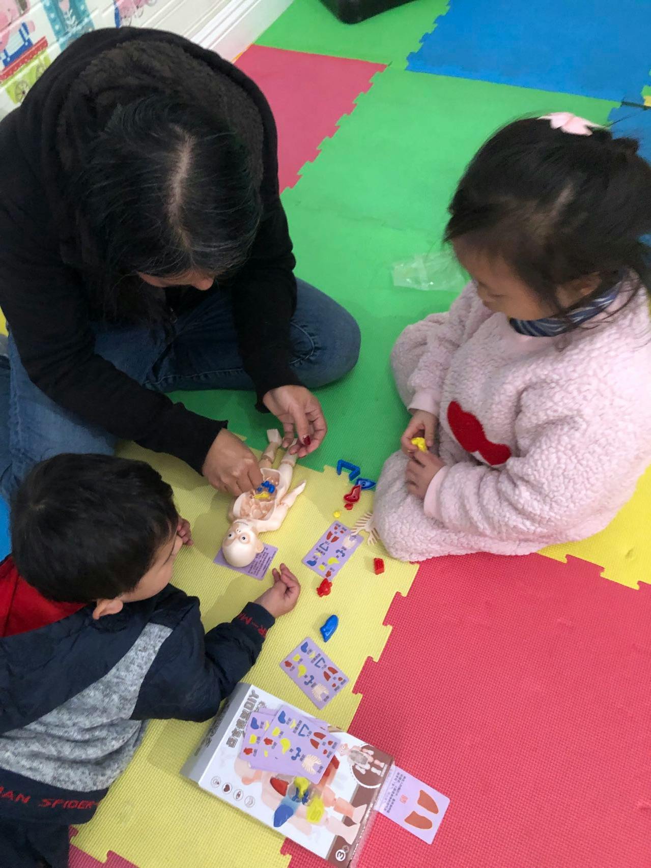 Person and two children playing with a doll and cards on a colorful mat