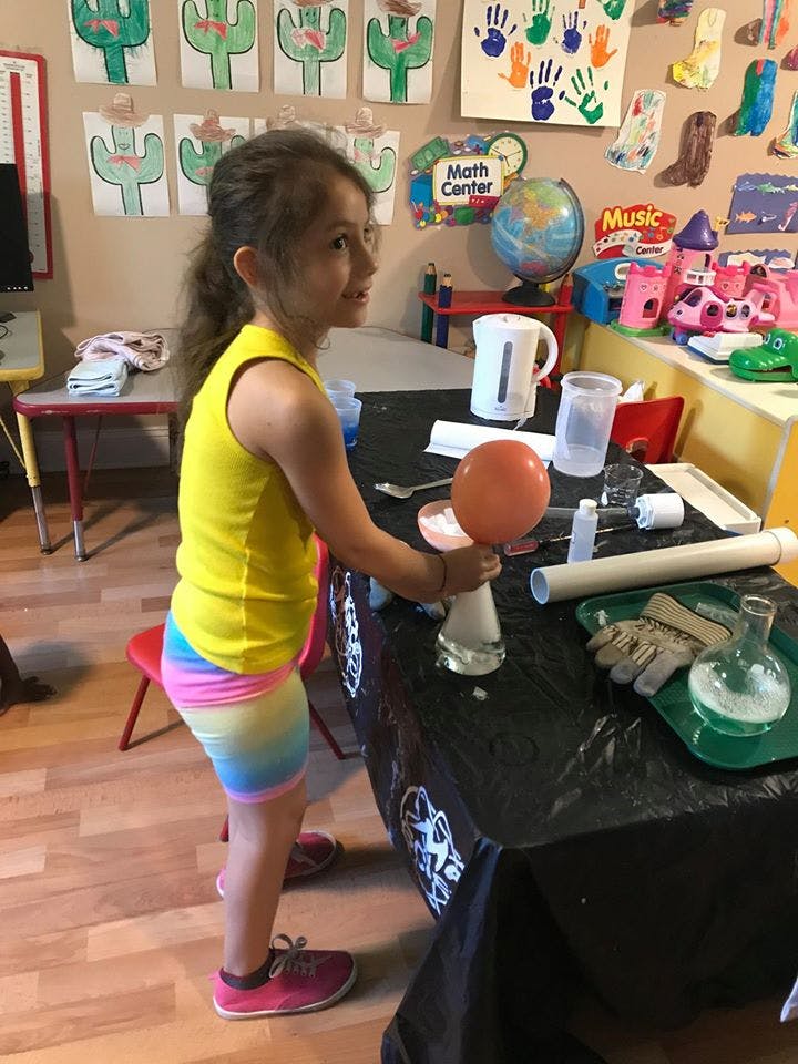 Child holding an orange balloon over a flask on a table