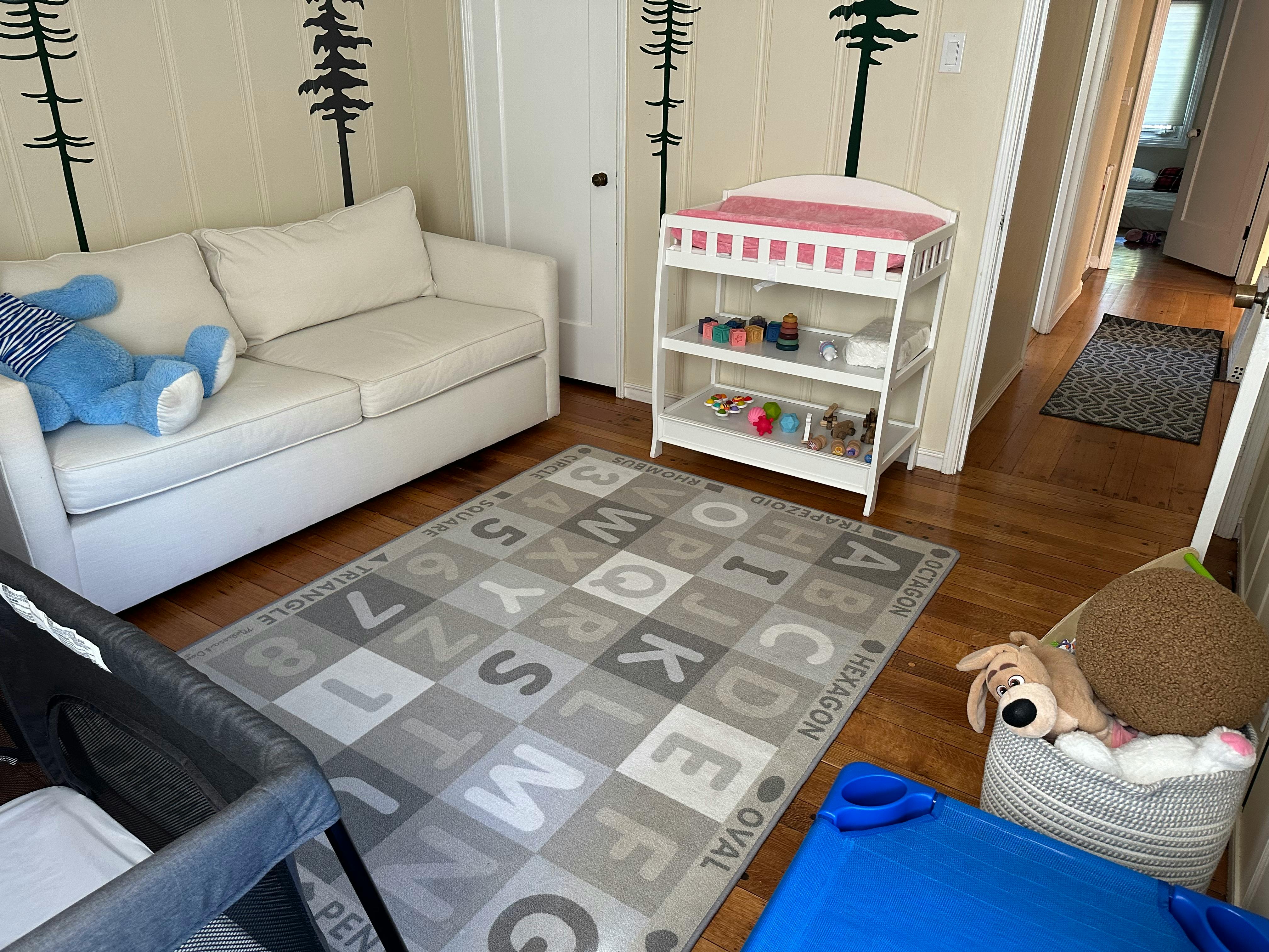 Nursery room with a white couch, changing table, and alphabet rug