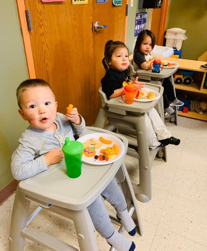 Three children sitting in high chairs with plates of food
