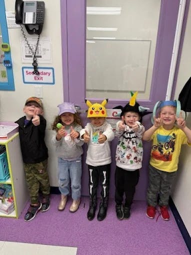 Five children in costumes giving thumbs up in a classroom