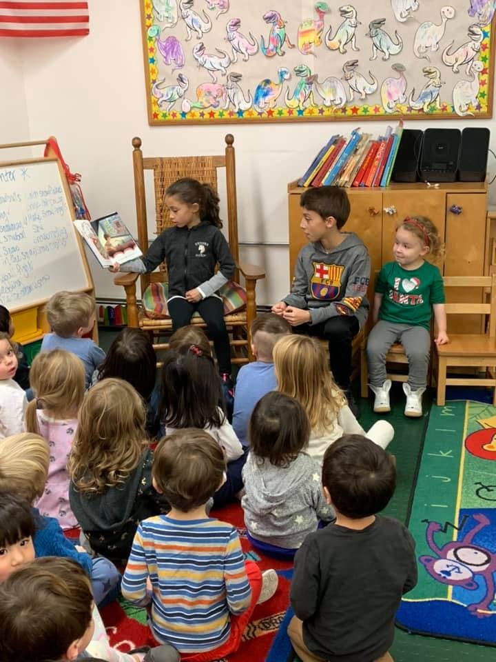 Child reading a book to other children in a classroom