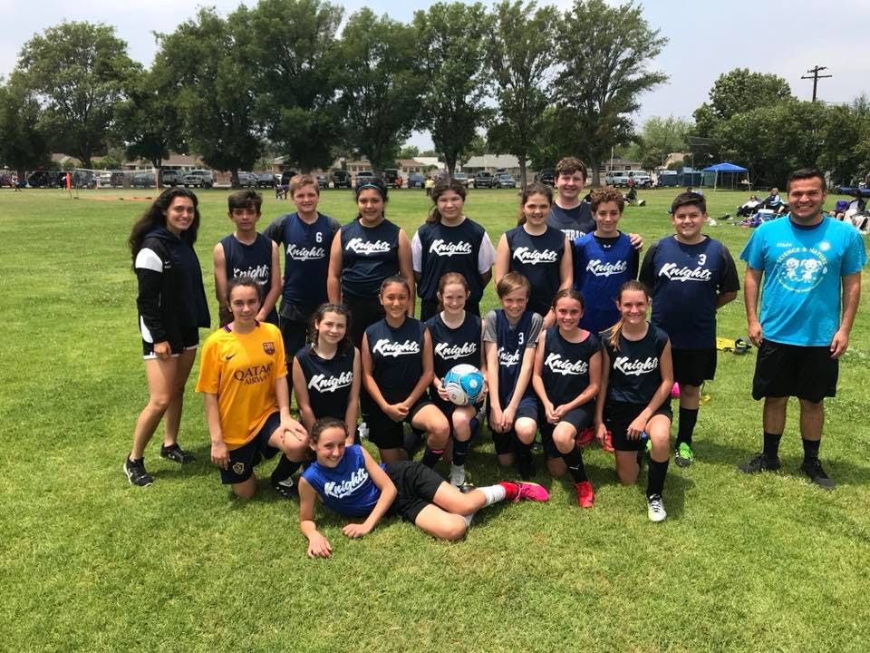 Group of teens and adults in sports attire posing on a grassy field