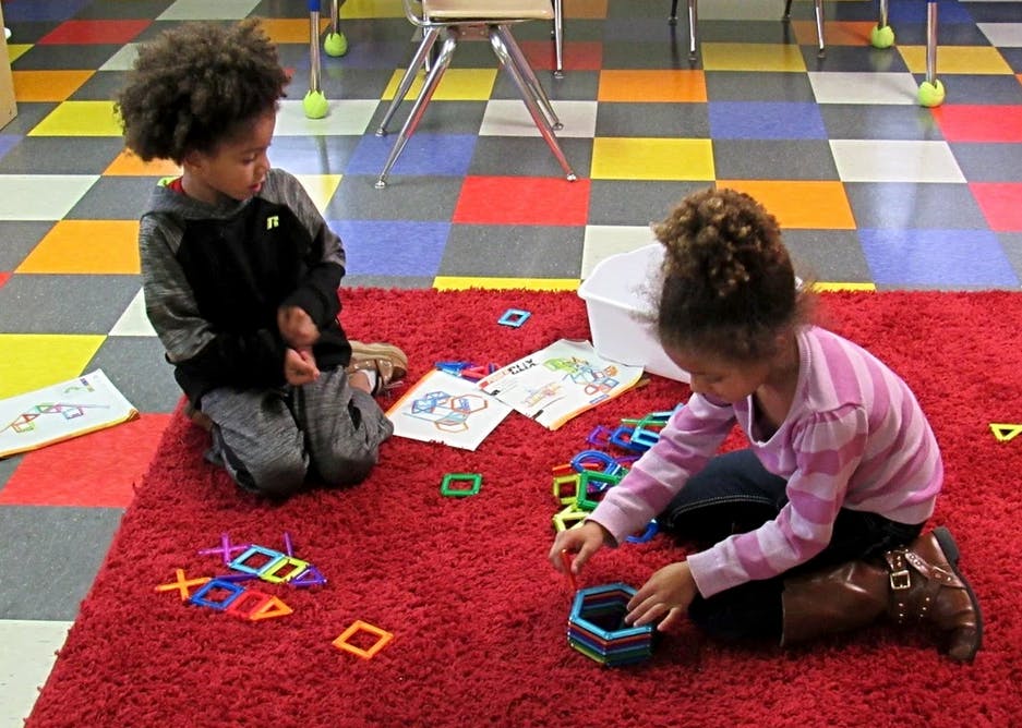 Two children playing with magnetic shapes on a red rug