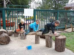 Three children playing on wooden logs outdoors