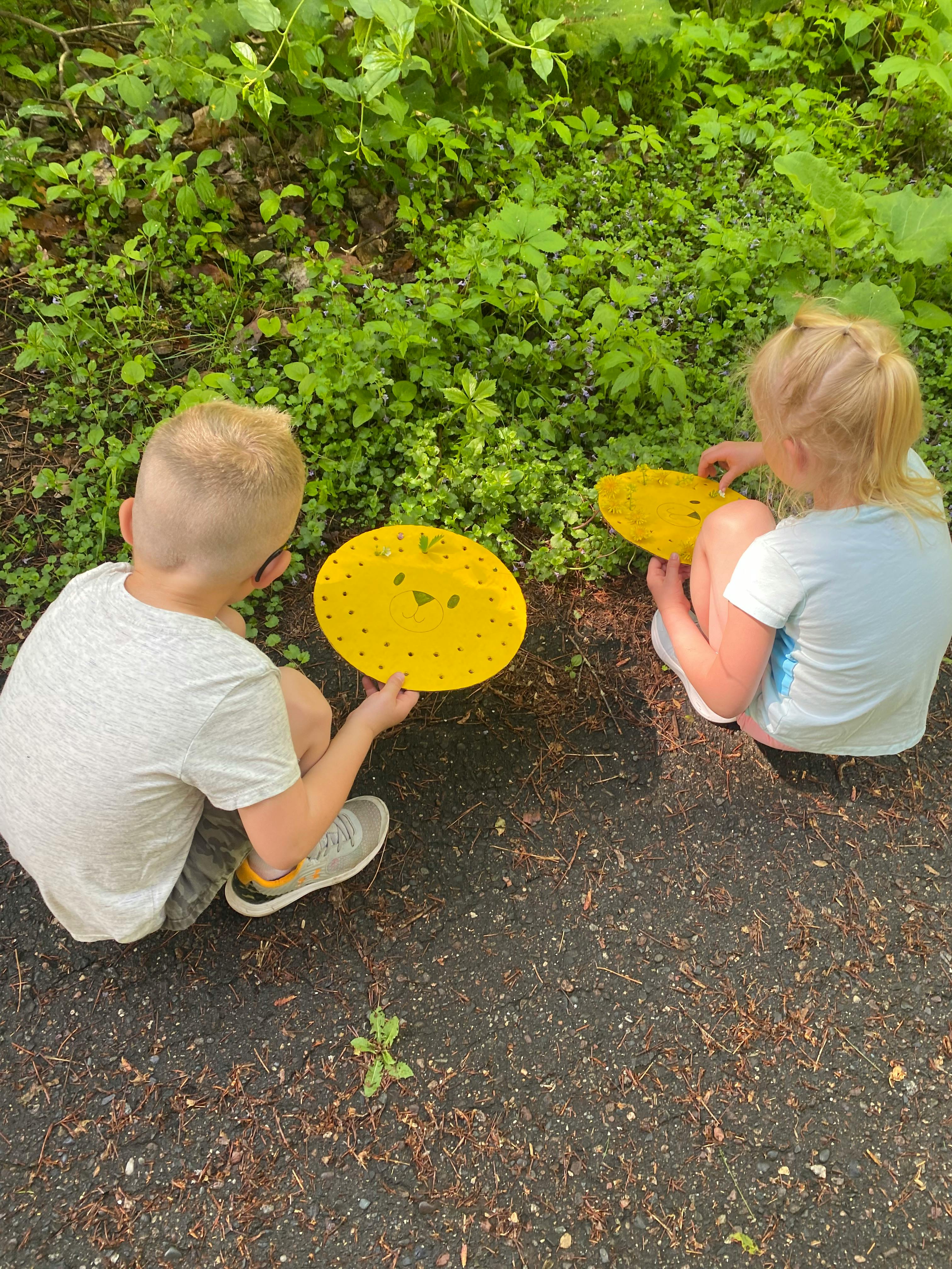 Two children holding yellow frisbees near green plants