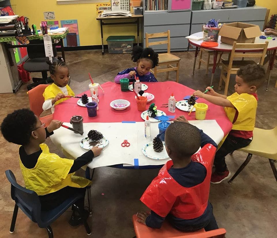 Children painting pinecones at a table