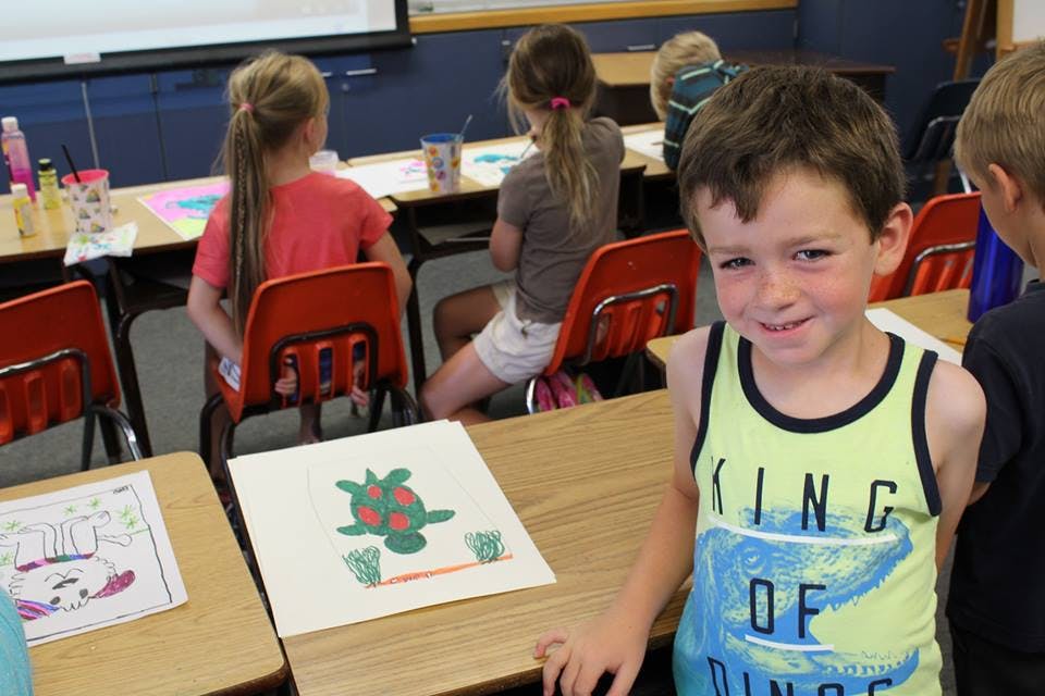 Child standing in a classroom with other children seated at desks