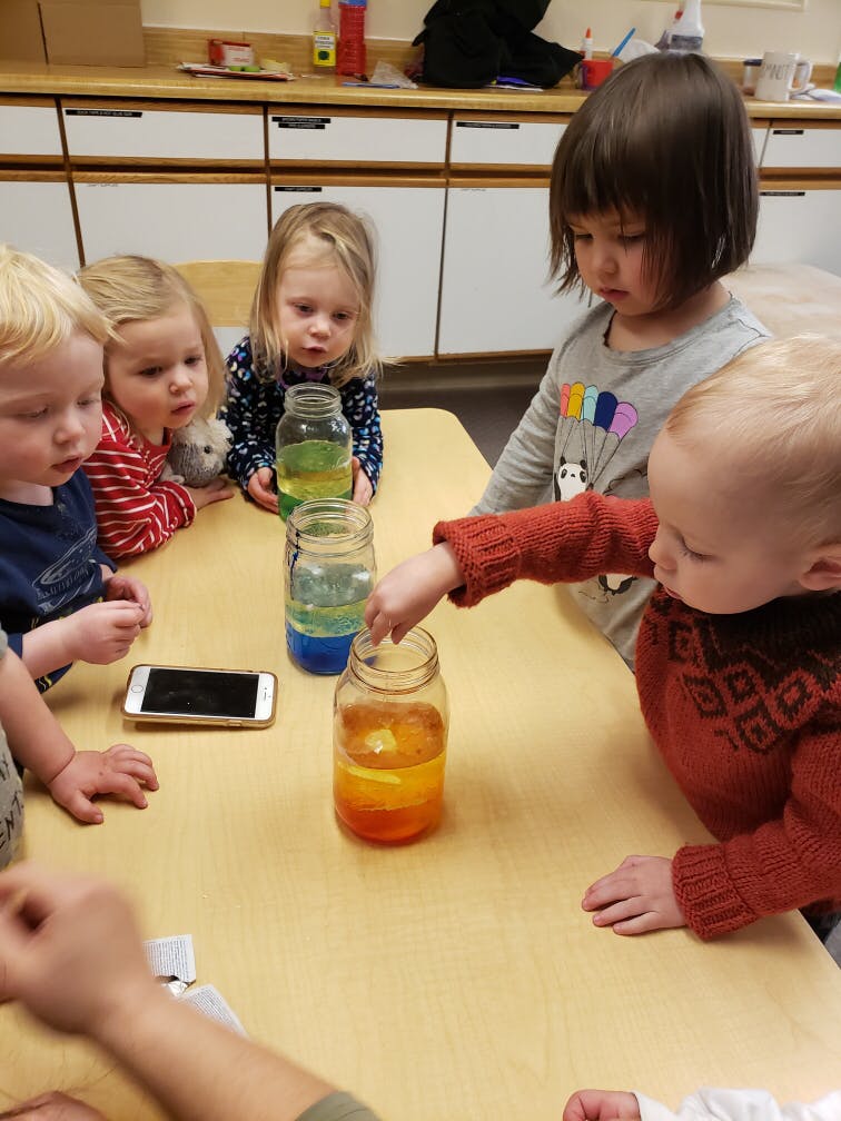 Children gathered around a table with jars of colorful liquid
