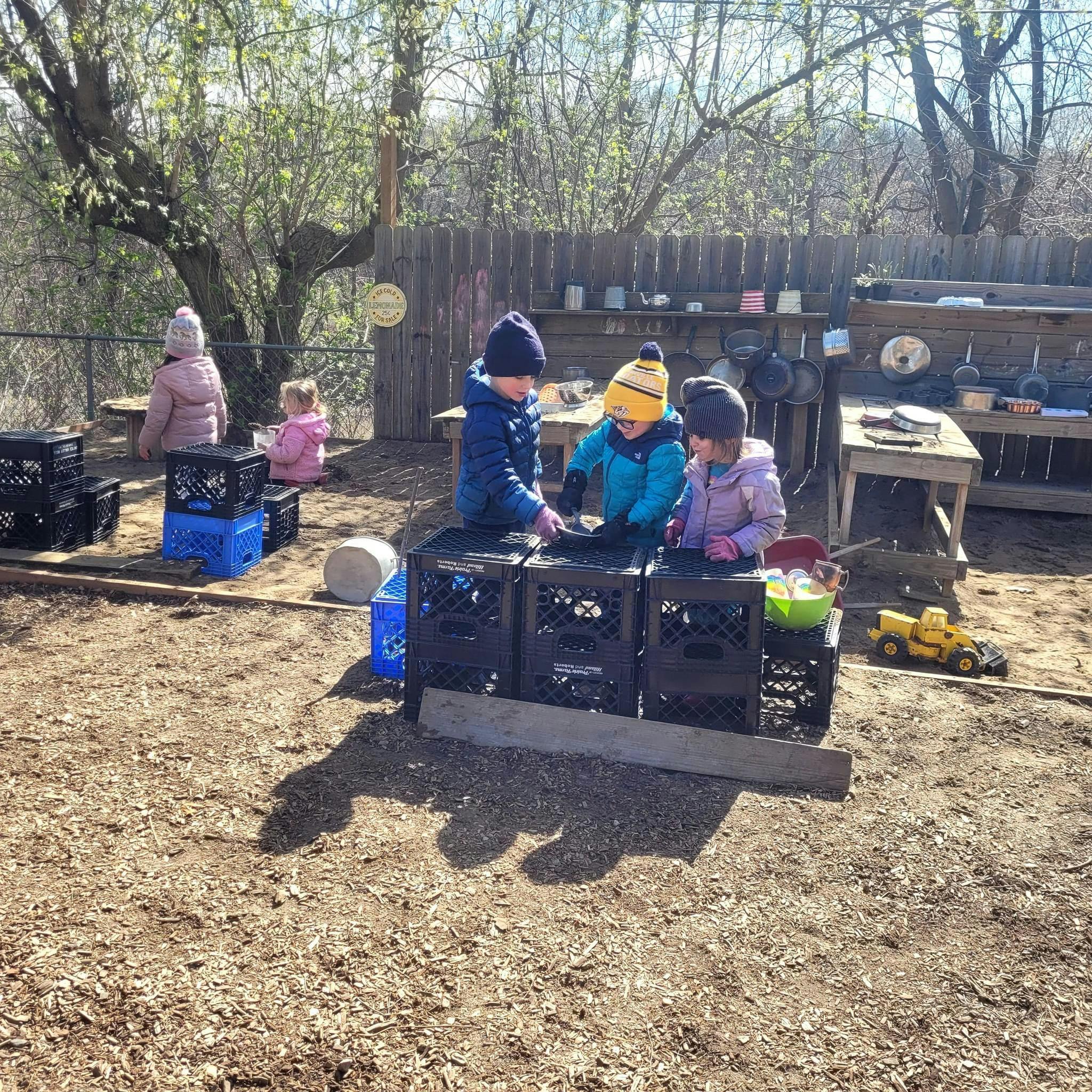 Three children playing with crates outdoors