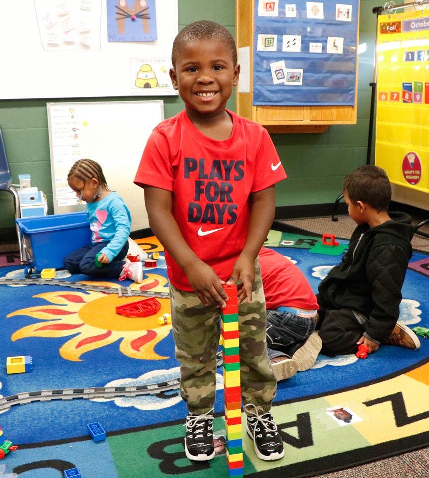 Child holding a tall stack of colorful blocks in a classroom