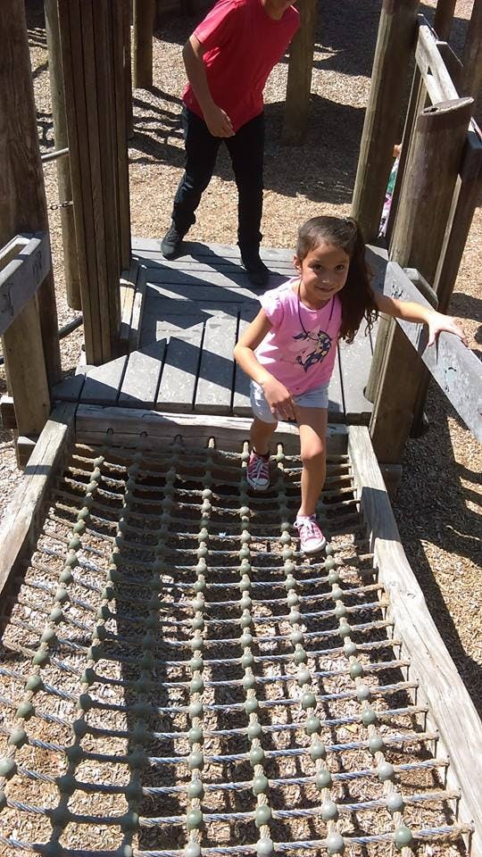 Child on a rope bridge on a playground, person in background