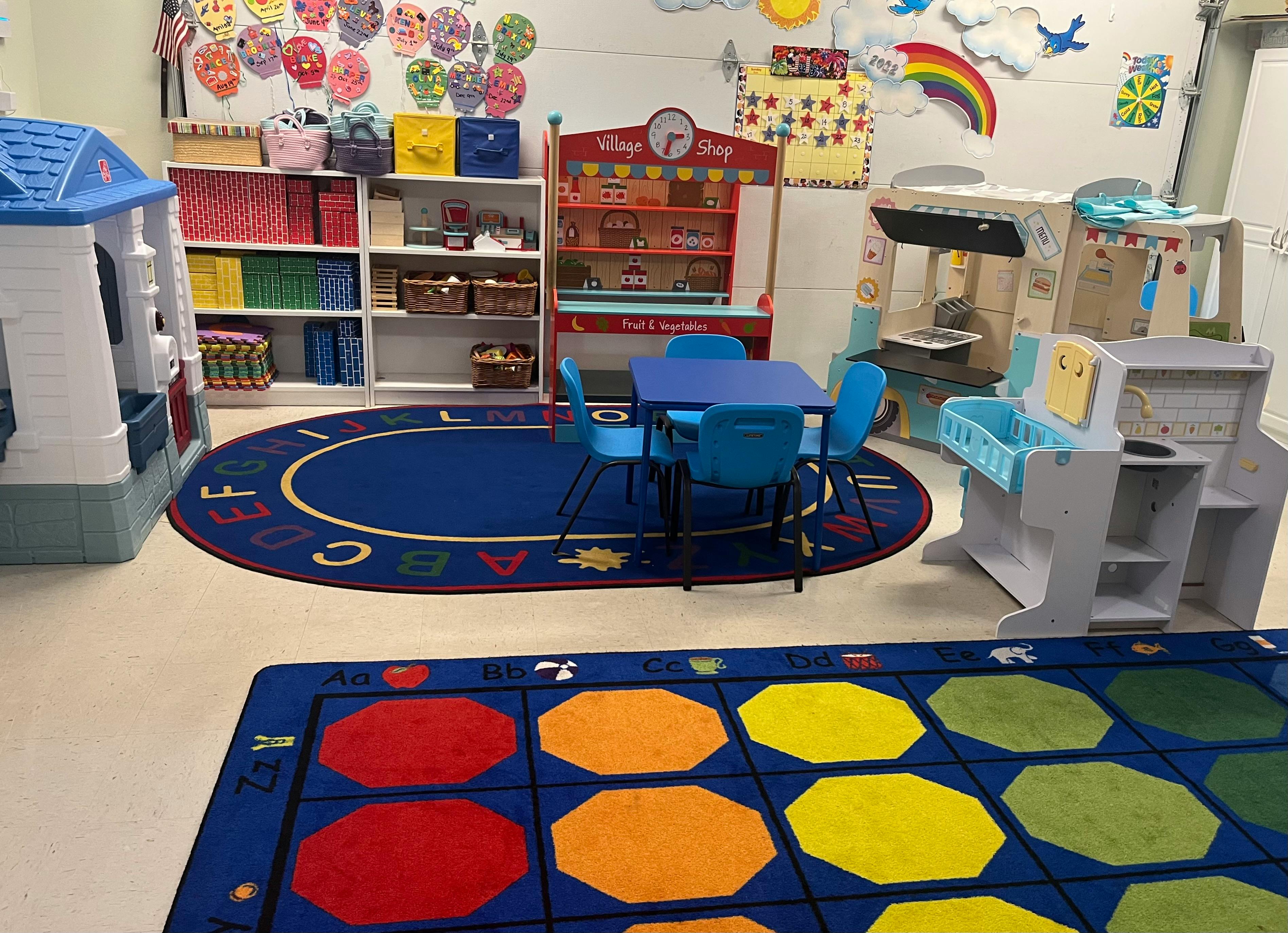 Playroom with blue table and chairs, toy kitchen, and colorful rugs
