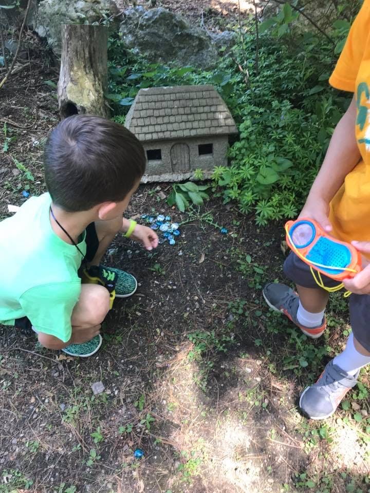 Child crouching near a small house model, another child holding a toy