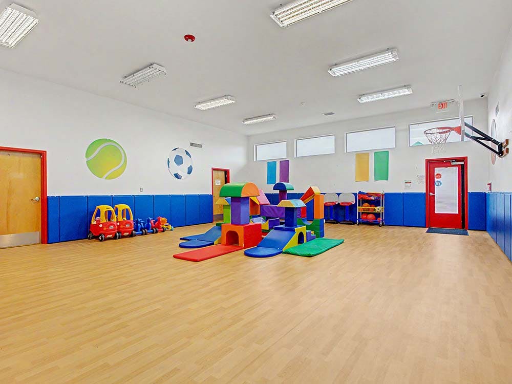 Indoor playroom with colorful soft play equipment, ride-on toys, and basketball hoop