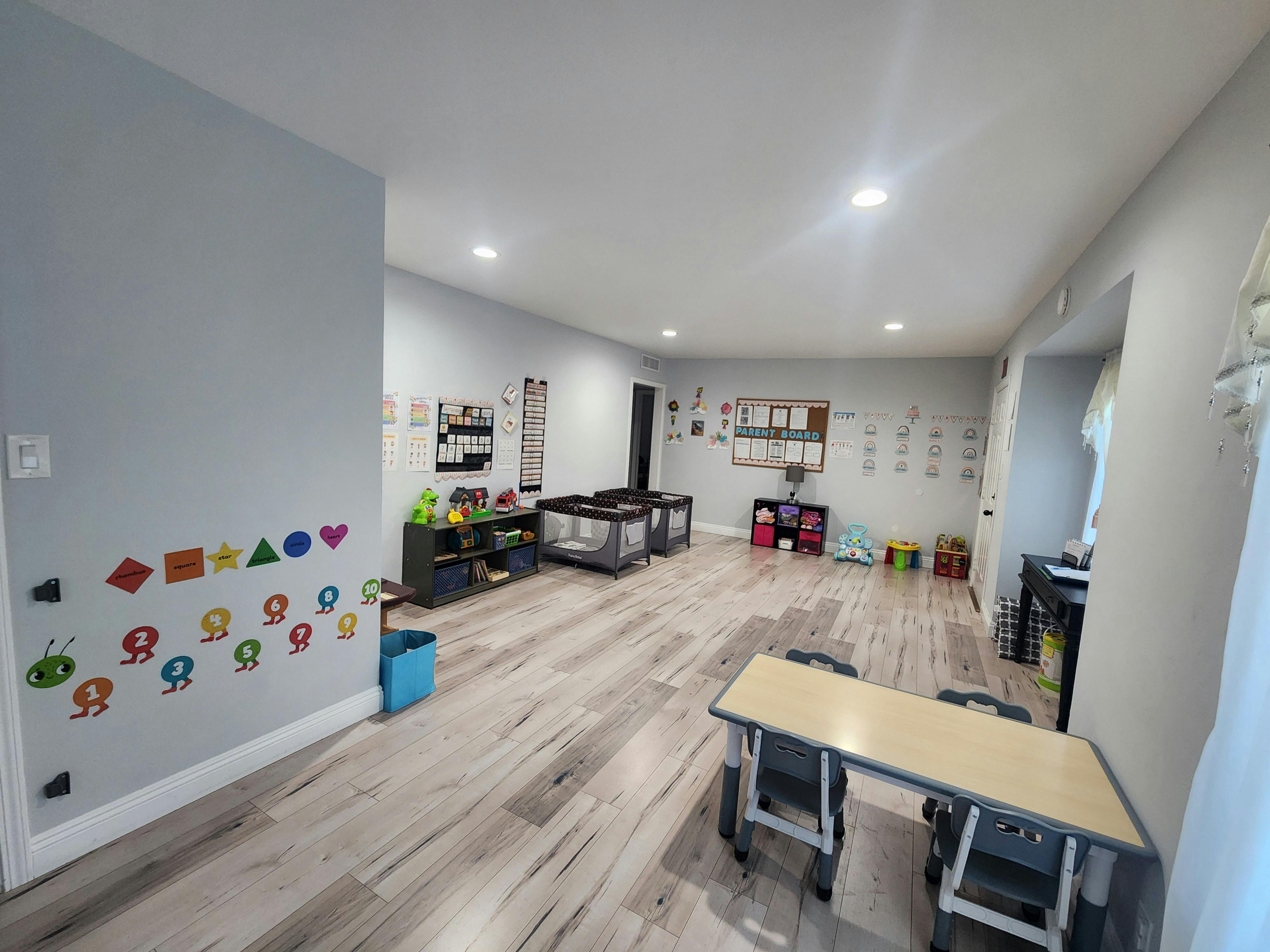 Empty classroom with small tables, cribs, and colorful wall decorations