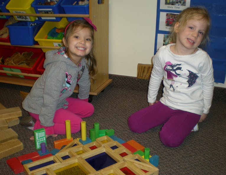 Two children kneeling on the floor with colorful building blocks