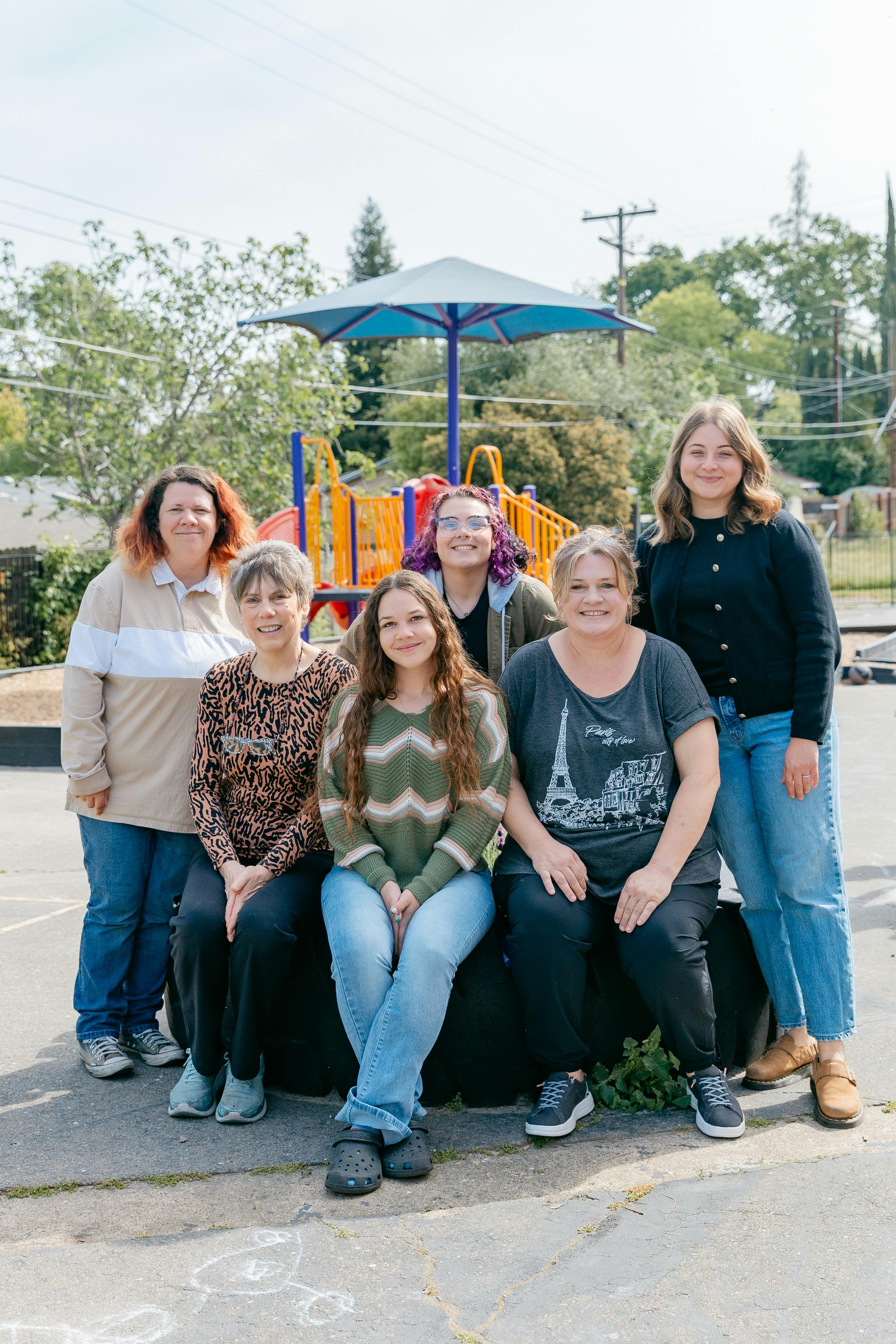 Six people posing for a photo outdoors with a playground in the background