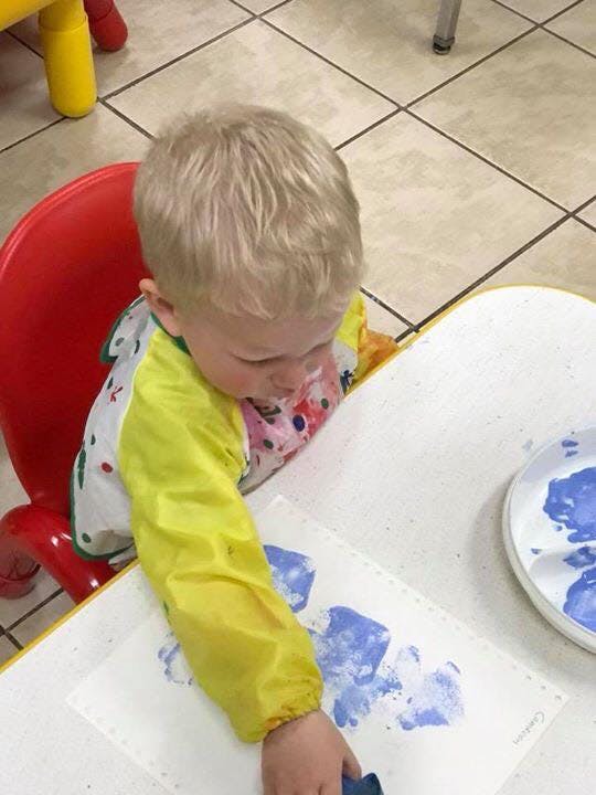 Child in a high chair painting with blue paint