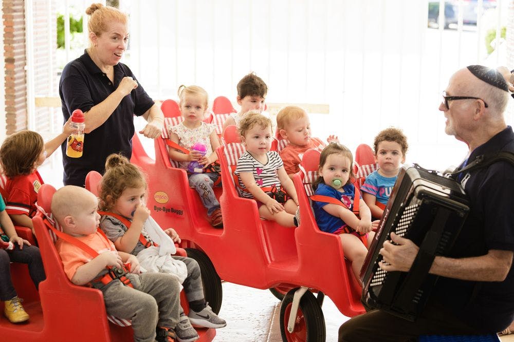 Adults with children in a multi-seat stroller and an adult playing an accordion