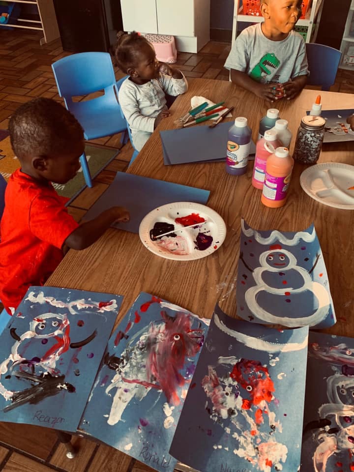 Children painting at a table with various art supplies