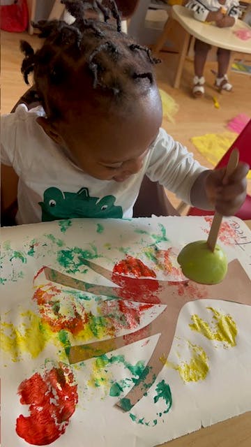Child painting with an apple on a stick