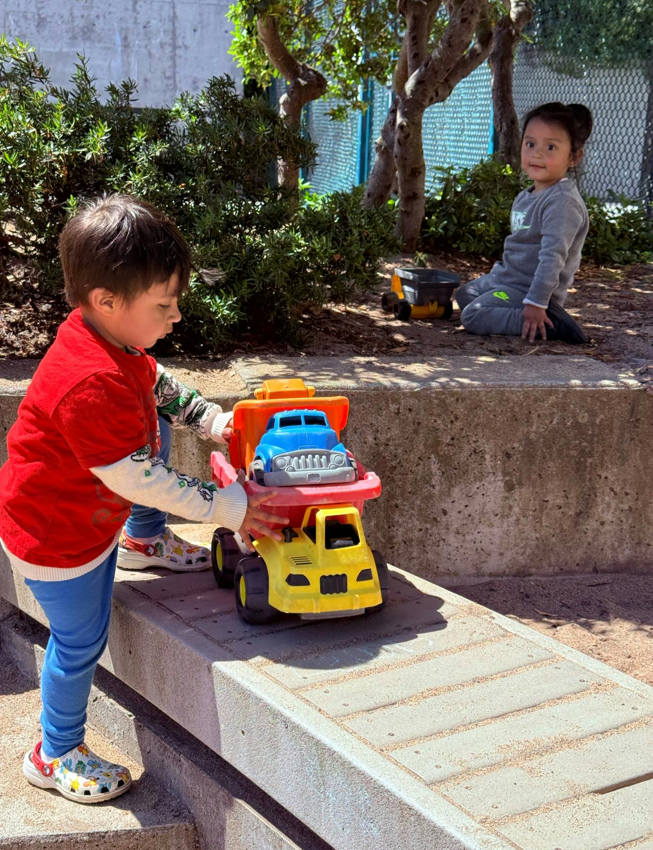 Child playing with toy truck, another child sitting in the background