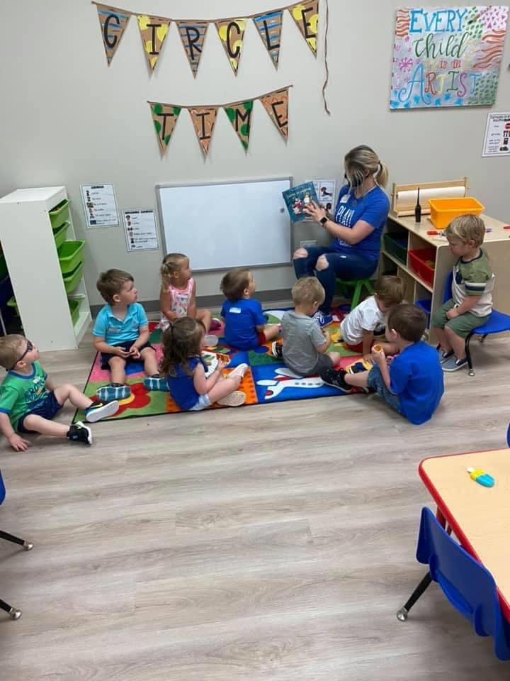 Adult reading a book to a group of children sitting on a rug in a classroom
