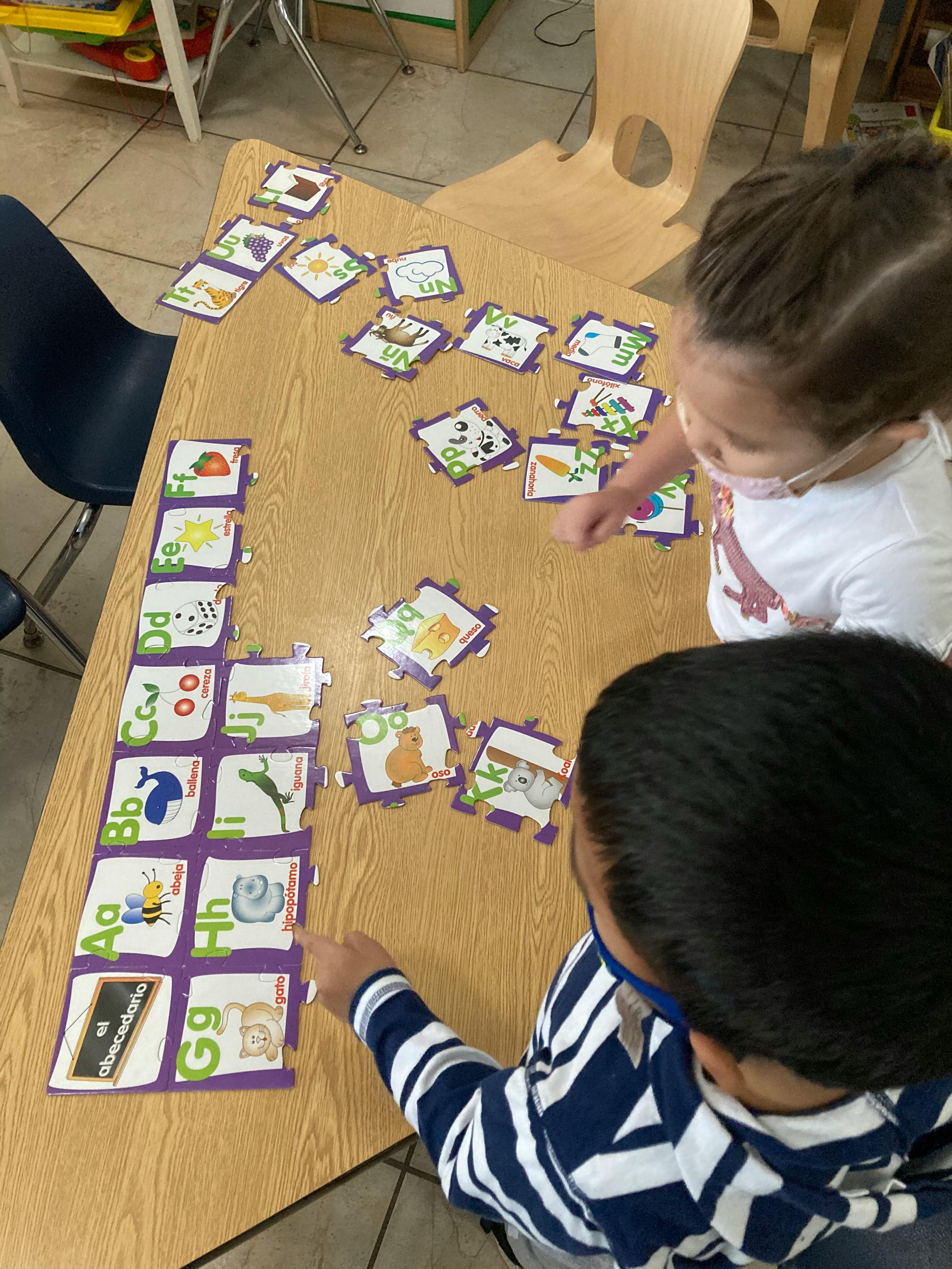 Two children playing with alphabet puzzle pieces on a table