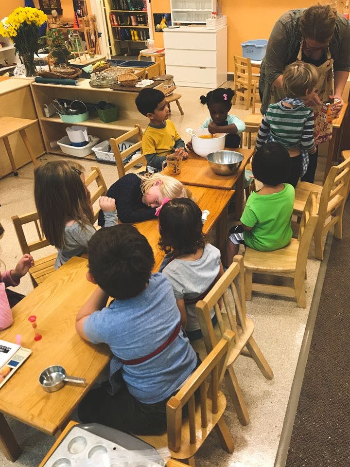Adult and children gathered around tables in a classroom