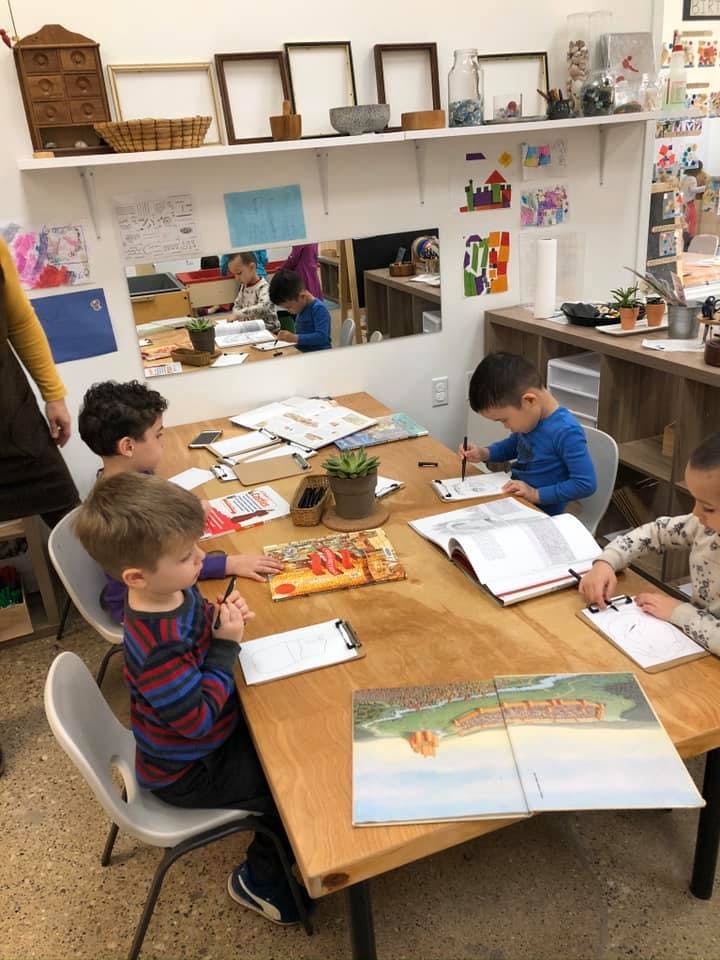 Children sitting at a table in a classroom, reading and writing