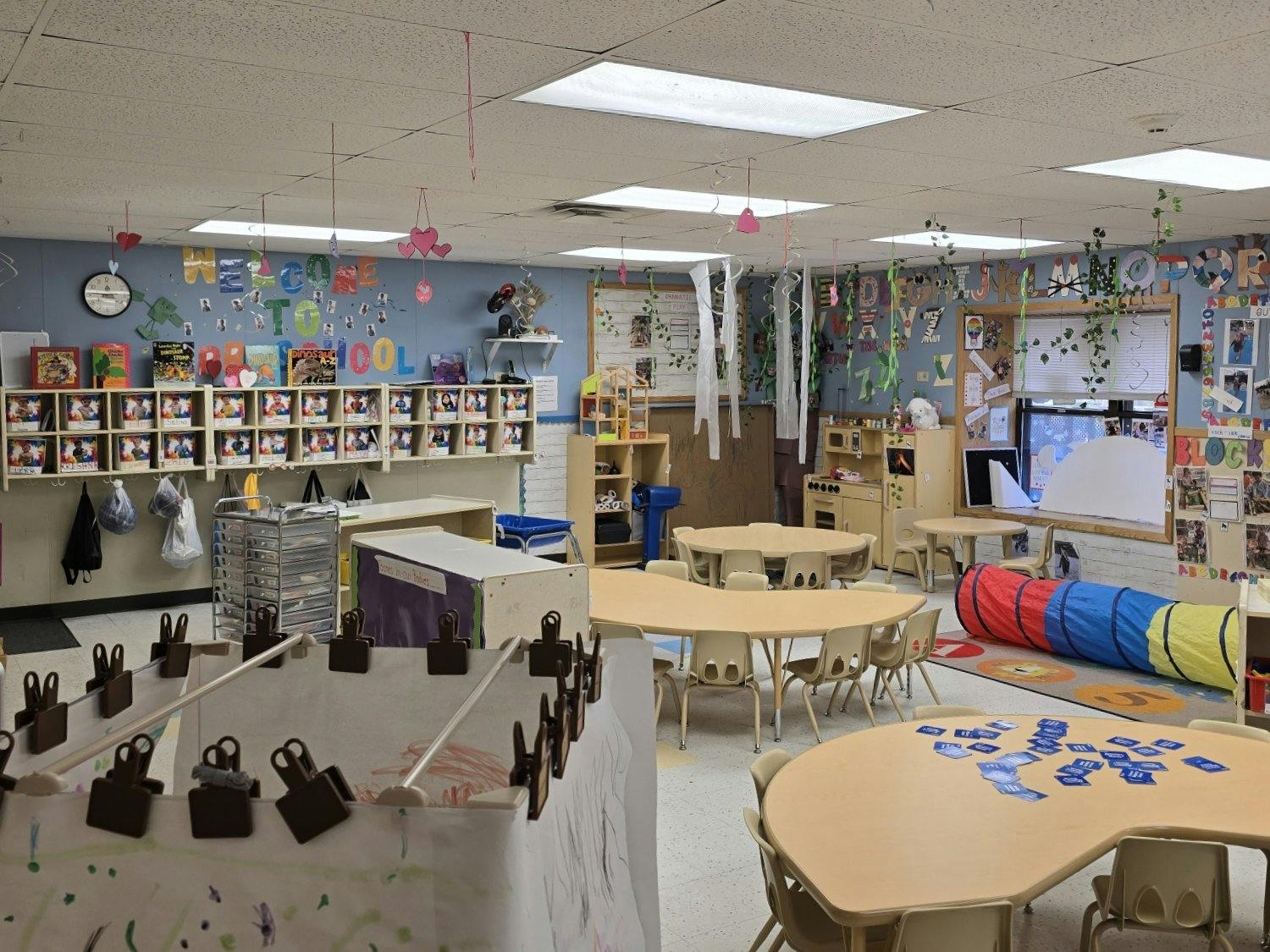 A colorful classroom with tables, chairs, cubbies, toys, and decorations