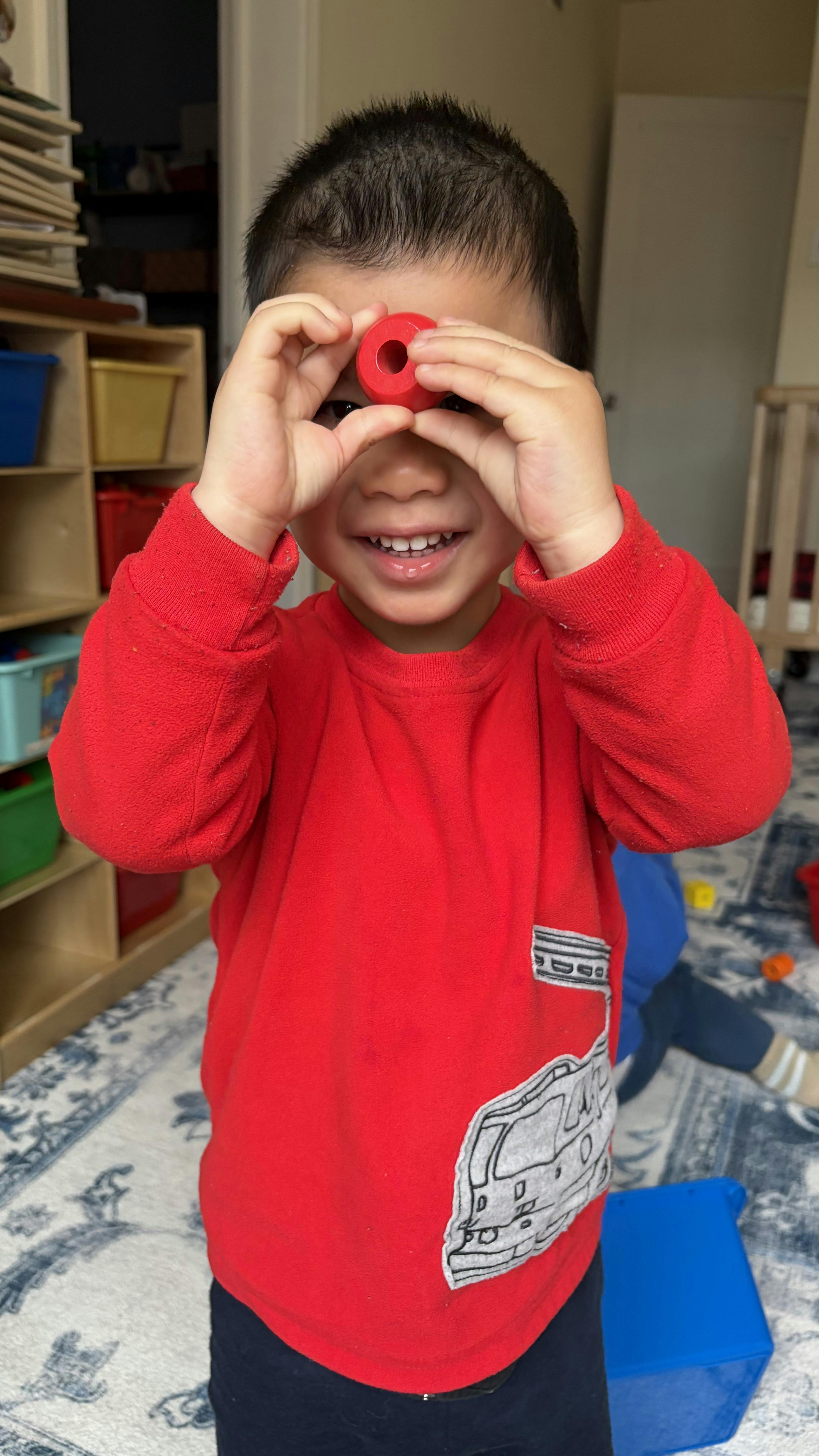 Child in red shirt holding a red toy ring over one eye