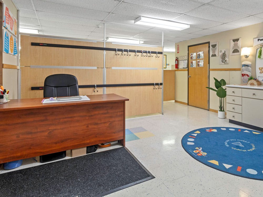 Desk with a black office chair and a blue circular rug in a classroom