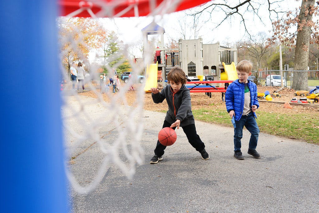 Child dribbling a basketball with another child standing nearby on a playground