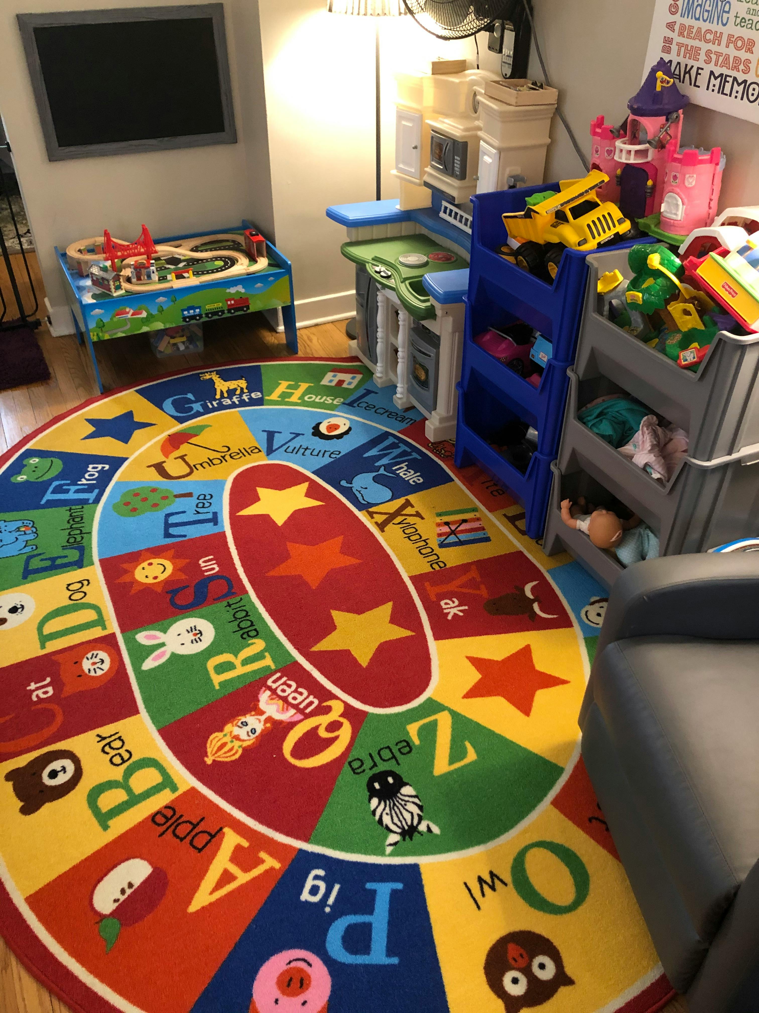 Playroom with an alphabet rug, toy kitchen, and train table