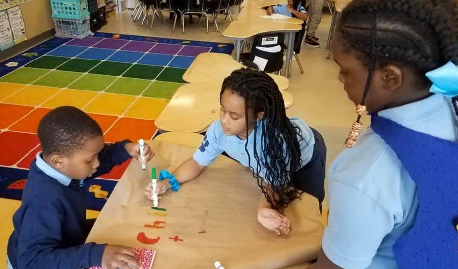 Three children working on a craft project at a table in a classroom