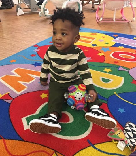 Child sitting on a colorful alphabet rug with a toy