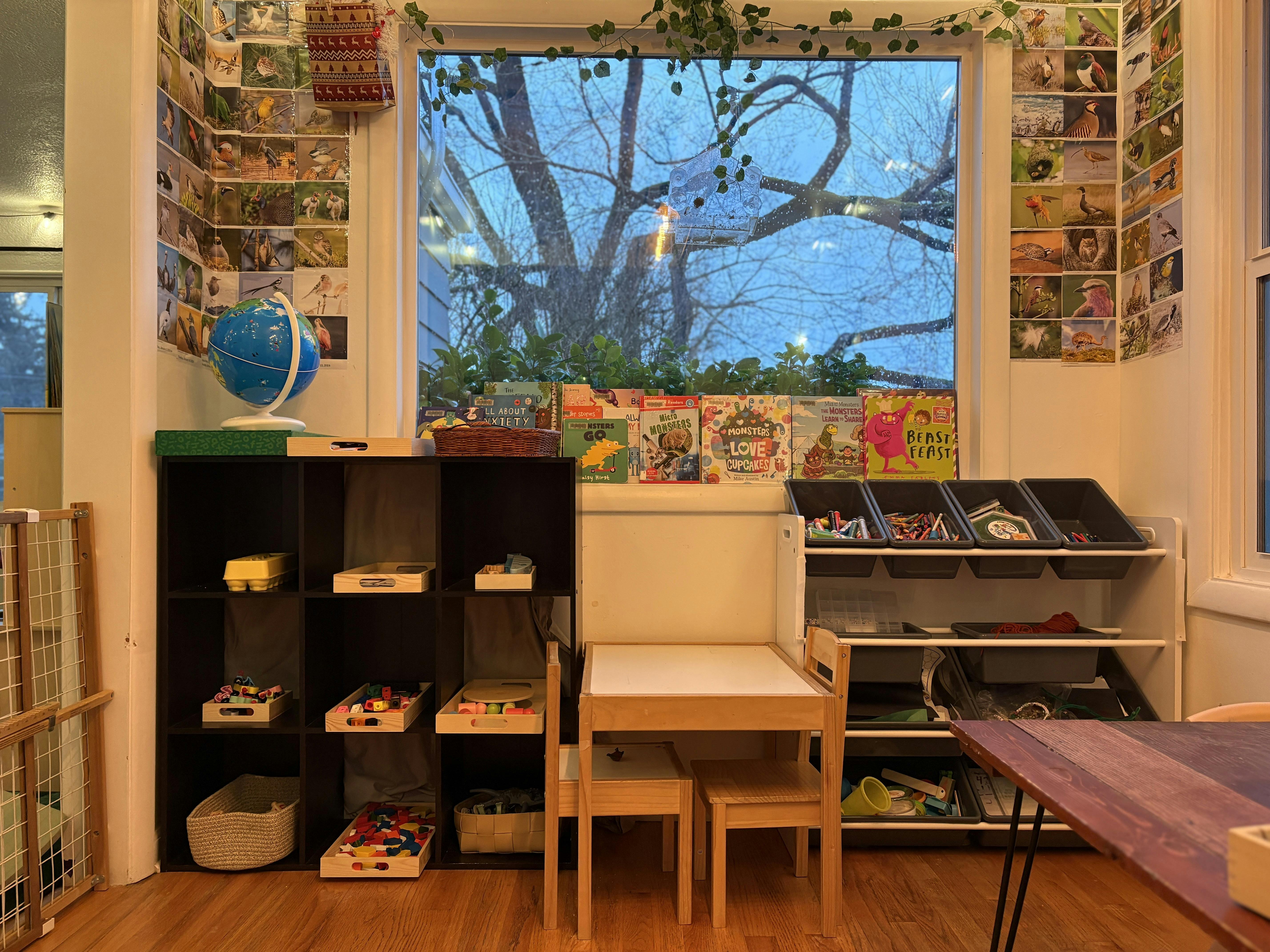 Children's play area with shelves of toys, books, and art supplies by a window