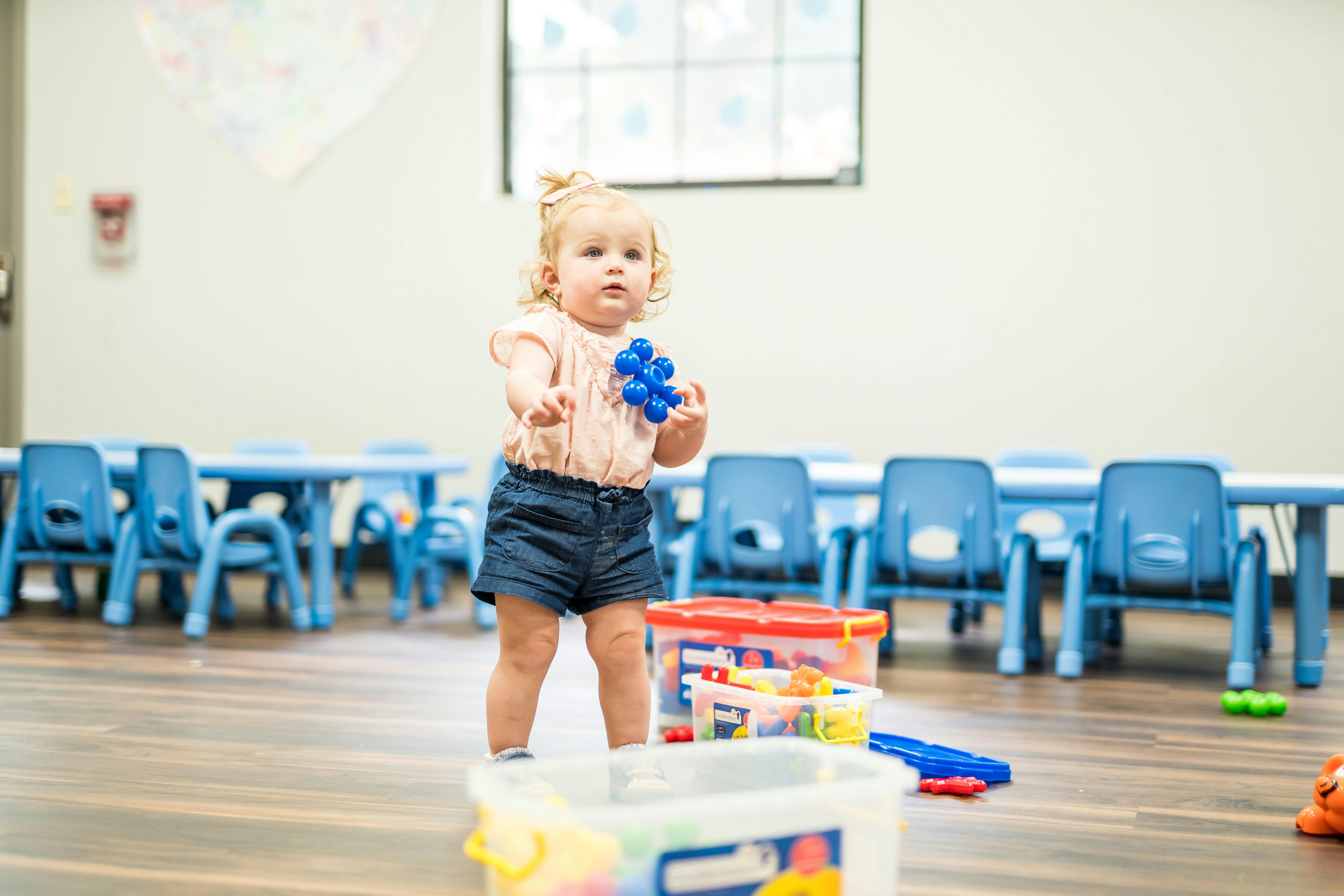 Child standing in a classroom holding a toy