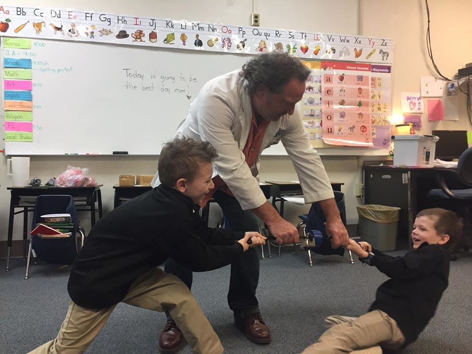 Person and two children playing tug-of-war with a rope in a classroom