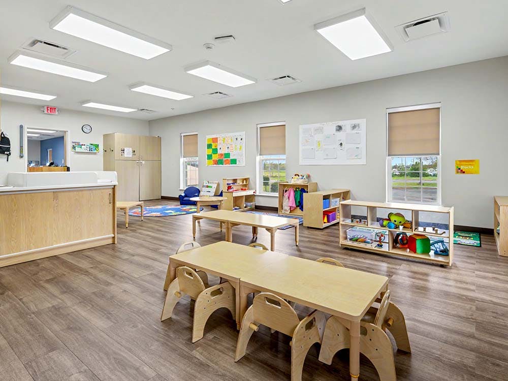 Classroom with small tables and chairs, shelves with toys, and bulletin boards