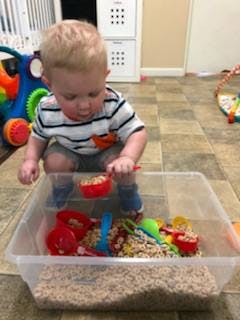 Child playing with sensory bin with scoops and small objects