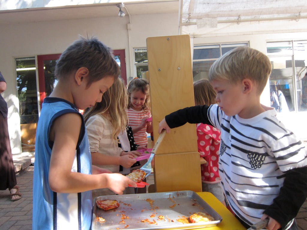 Two children serving food from a tray with spatulas