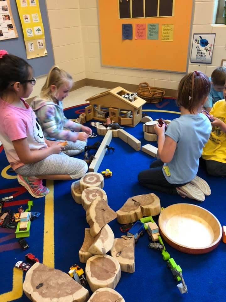 Children playing with wooden blocks and a toy barn on a blue rug