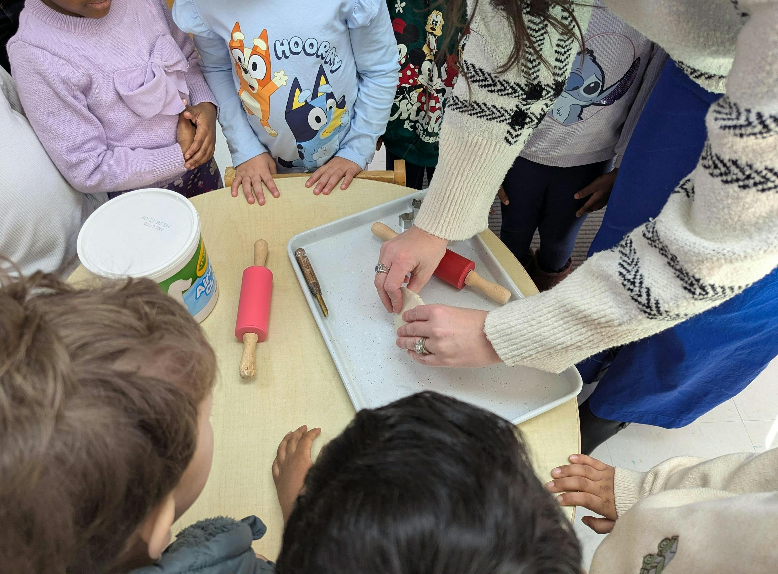 Adult and group of children using rolling pins to work with dough at a table